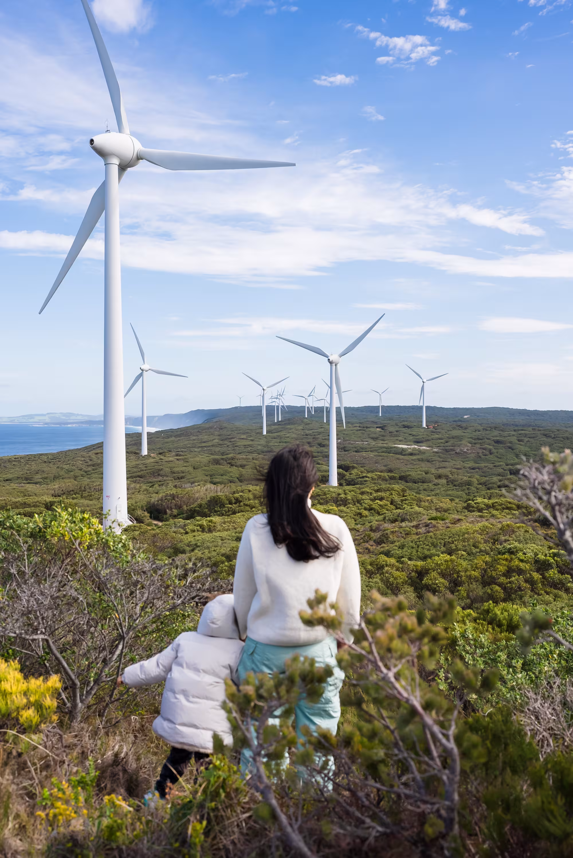 Mother and child with their back to the camera facing wind turbines 