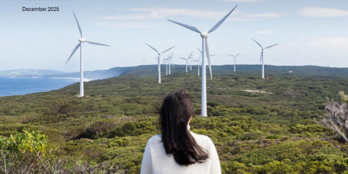 Woman and child on a green mountain side with their backs turned to us, looking at a horizon with wind turbines.